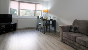 Un salon moderne avec un téléviseur à écran plat, une table à manger avec des chaises, un canapé et une lampe.