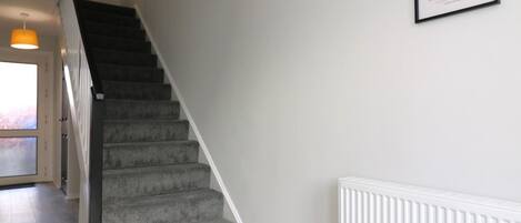 A staircase with carpeted steps leading to a landing, a white radiator, and a framed artwork on the wall.