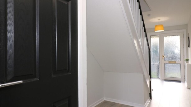 Un couloir avec une porte noire, un escalier et une suspension jaune.