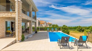 A two-story house with a swimming pool, outdoor seating, and a view of the countryside.