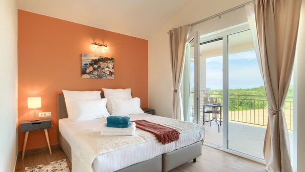 A bedroom with a bed, a nightstand, a painting, and a balcony with a view.