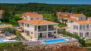 A residential area with houses featuring red-tiled roofs, a swimming pool, and a landscaped garden.