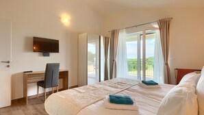 A hotel room with a bed, a desk, a chair, a TV, and a balcony with curtains.