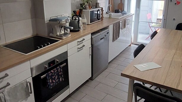 Une cuisine moderne avec des armoires blanches, un plan de travail en bois, un four encastré et un coin repas comprenant une table et des chaises.