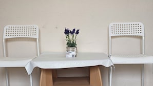 A room with two white chairs, a small table with a white tablecloth, and a vase with purple flowers.
