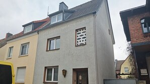 A two-story residential building with a grey facade, a small balcony, and a door with a window.