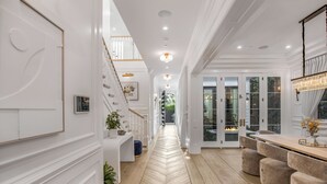 A spacious hallway with a wooden herringbone floor, white walls, and a staircase on the left.