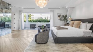 A modern bedroom with a large bed, a chandelier, and a view of the outdoors.