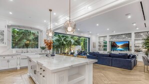 A spacious kitchen with a large island, white cabinetry, and a view of lush greenery.