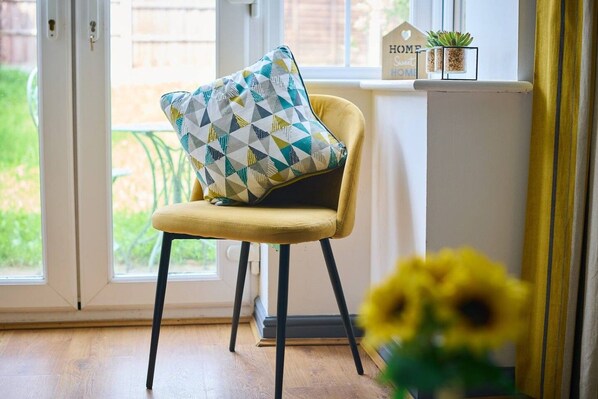 A chair with a geometric patterned cushion, a small potted plant, and a sign with 'HOME Sweet HOME' on a window sill.
