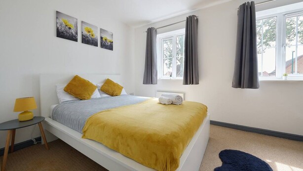 Ein Schlafzimmer mit einem Bett, einem Nachttisch, einer Lampe, einem Fenster mit Vorhängen und Wandbildern.