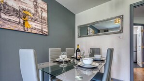 Ein Essbereich mit einem Glastisch, weißen Stühlen und einem Bild an der Wand.