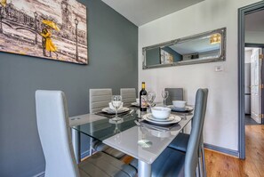Un comedor con una mesa de vidrio, sillas blancas y un cuadro en la pared.