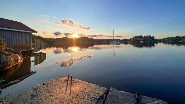 Ein ruhiger See bei Sonnenuntergang mit einem Steg und einem Gebäude auf der linken Seite.