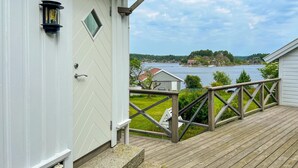 Eine Holzterrasse mit Geländer, eine weiße Tür mit Fenster und ein Blick auf einen See sowie Häuser in der Ferne.