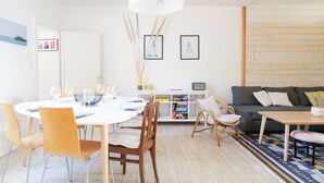 A modern living room with a dining area, featuring a round table, wooden chairs, a sofa, and a bookshelf. - Holiday home quartier Arago Les Sables - 8 people (Les Sables-d´Olonne)