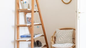 A wooden ladder shelf with books and decorative items, a wicker chair with a cushion, and a framed picture on the wall. - Holiday home quartier Arago Les Sables - 8 people (Les Sables-d´Olonne)