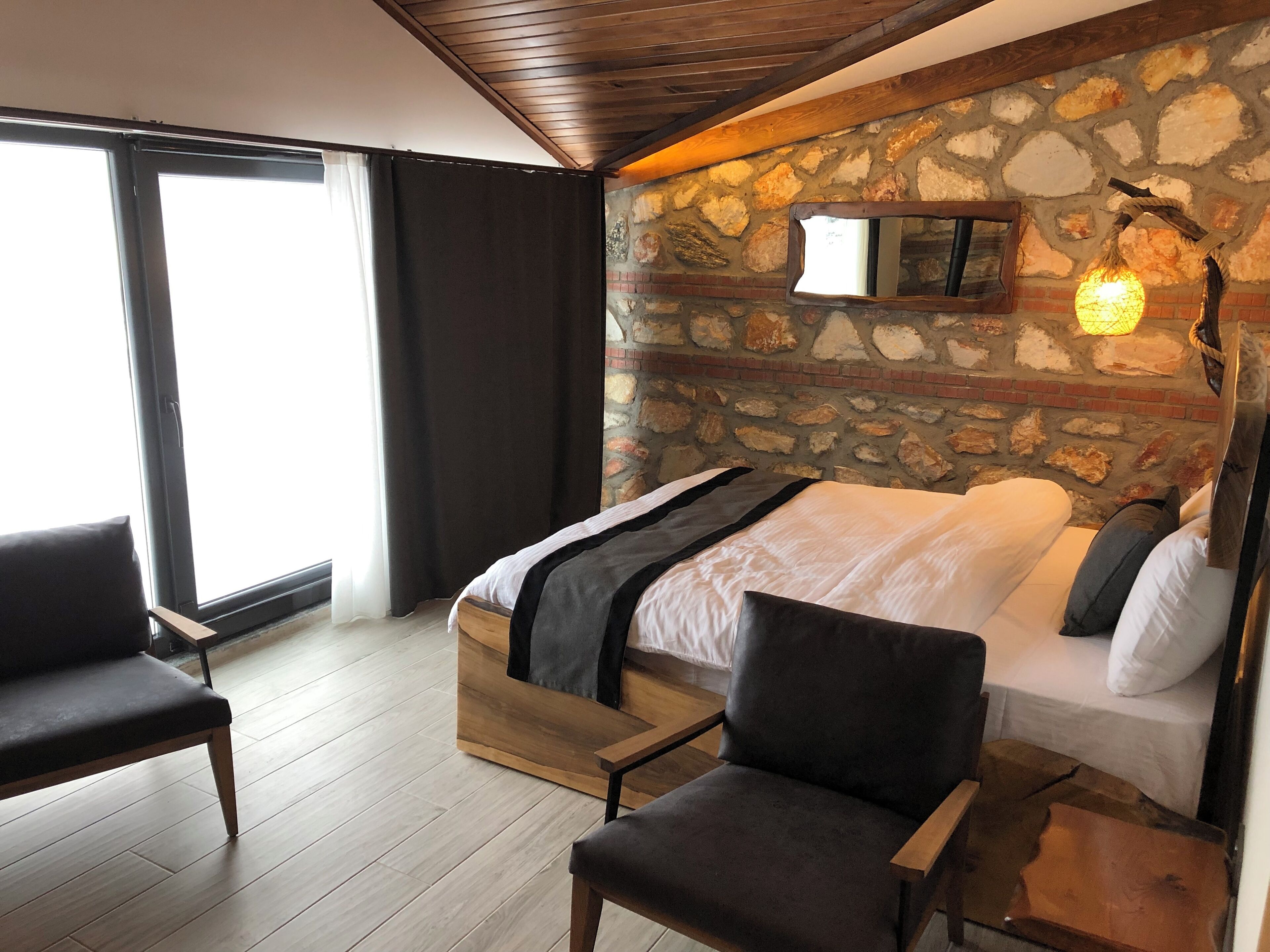 Un dormitorio con pared de piedra, una cama, un banco de madera y una silla.