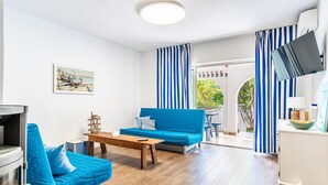 Een moderne woonkamer met een blauwe bank, een houten salontafel en een aan de muur bevestigde televisie.