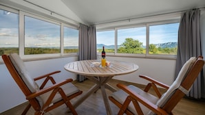 Un balcon avec une table ronde en bois, quatre chaises en bois, une bouteille de vin et un verre de jus d’orange.