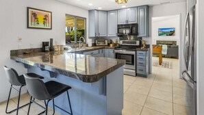 A modern kitchen with grey cabinets, a central island with bar stools, a microwave, oven, and a refrigerator.