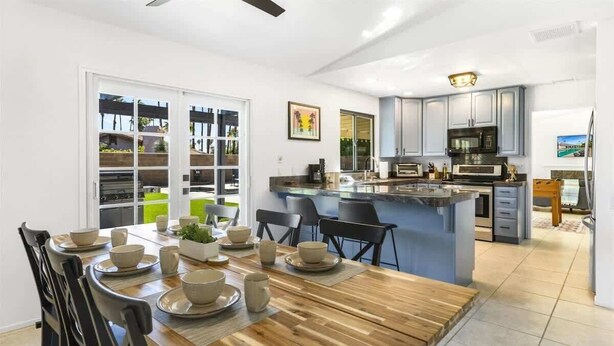 A modern kitchen with a central island, a dining area with a wooden table and chairs, and a view of the outdoors through large sliding doors.