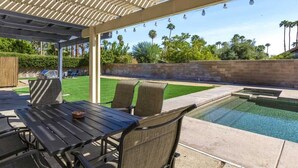 An outdoor patio with a pool, covered seating, and a view of the surrounding landscape.