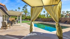 A pool area with a covered seating area, lounge chairs, and a pergola.