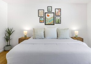 Quarto com uma cama grande, duas mesas de cabeceira com luminárias, um vaso de planta e obras de arte na parede.