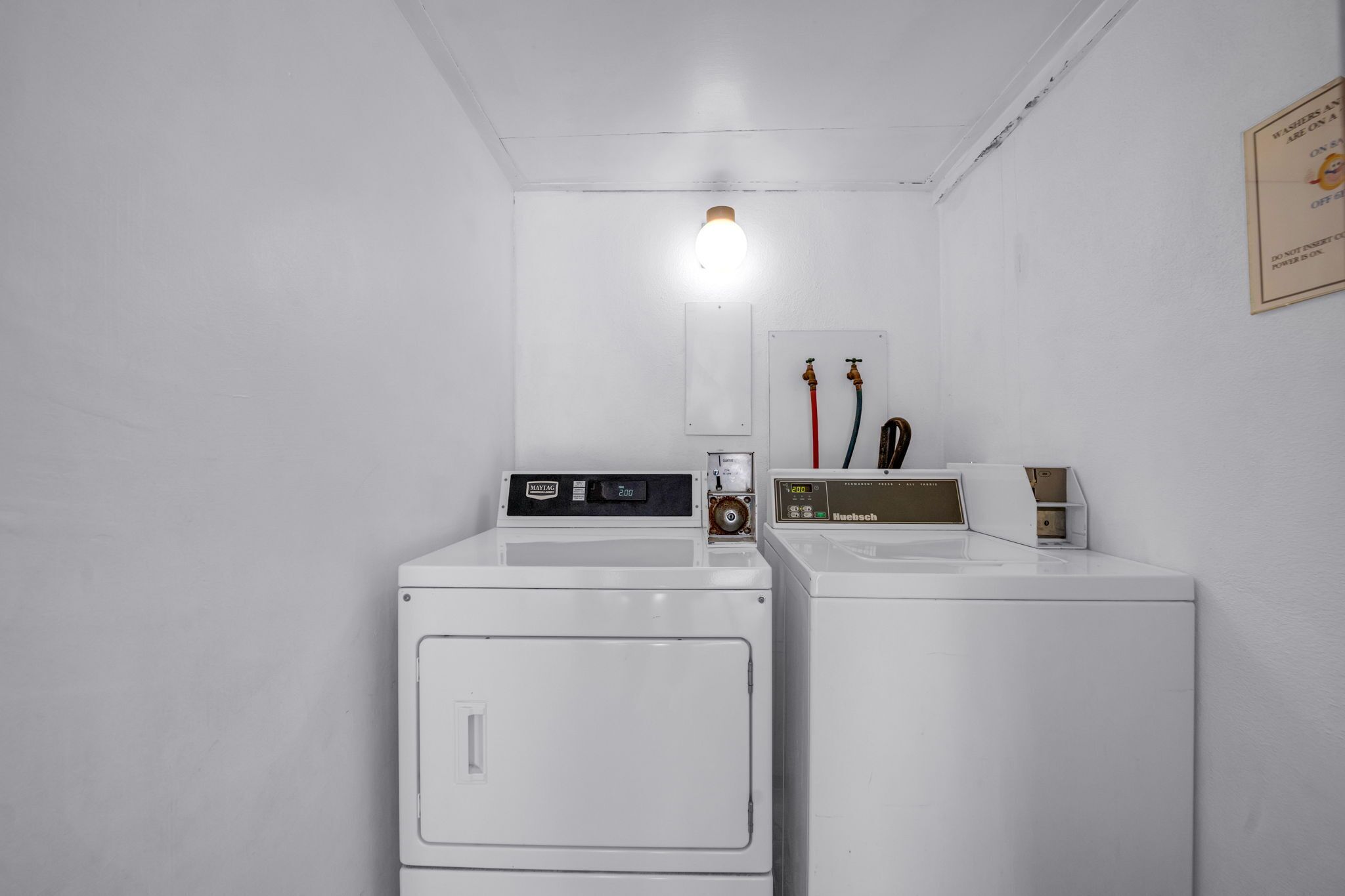 Een wasserette met twee witte wasmachines, een lamp en een bord aan de muur.