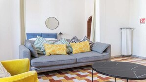 Een moderne woonkamer met een grijze bank, gele en gemêleerde kussens, een ronde spiegel en een zwarte salontafel.