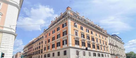 A multi-story building with a classical architectural style, featuring a central entrance with a canopy, multiple windows, and a corner location with a rounded corner.