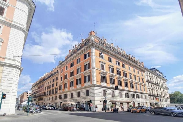 A multi-story building with a classical architectural style, featuring a central entrance with a canopy, multiple windows, and a corner location with a rounded corner.