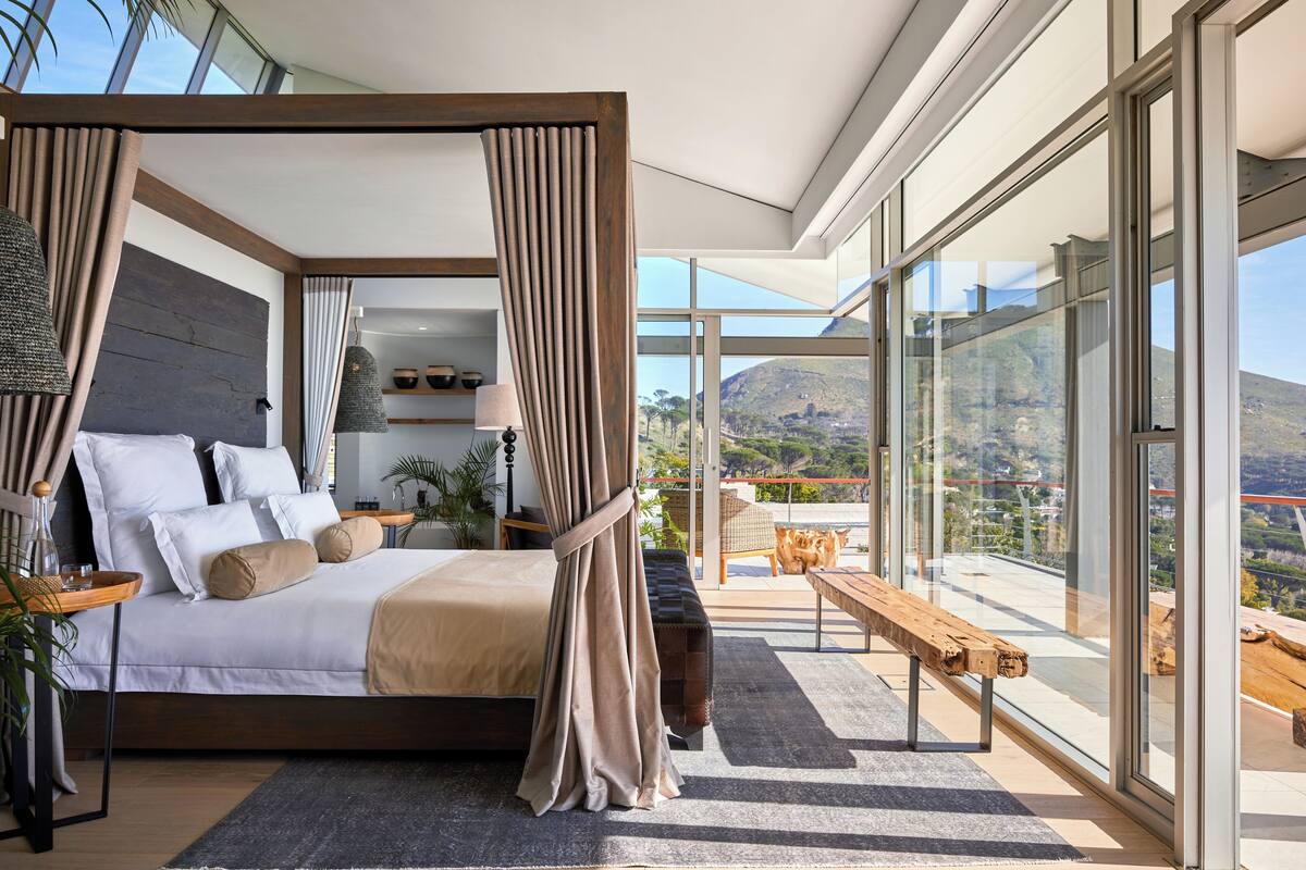 Ein modernes Schlafzimmer mit Baldachinbett, großen Fenstern und einem Balkon mit Blick auf die Landschaft.