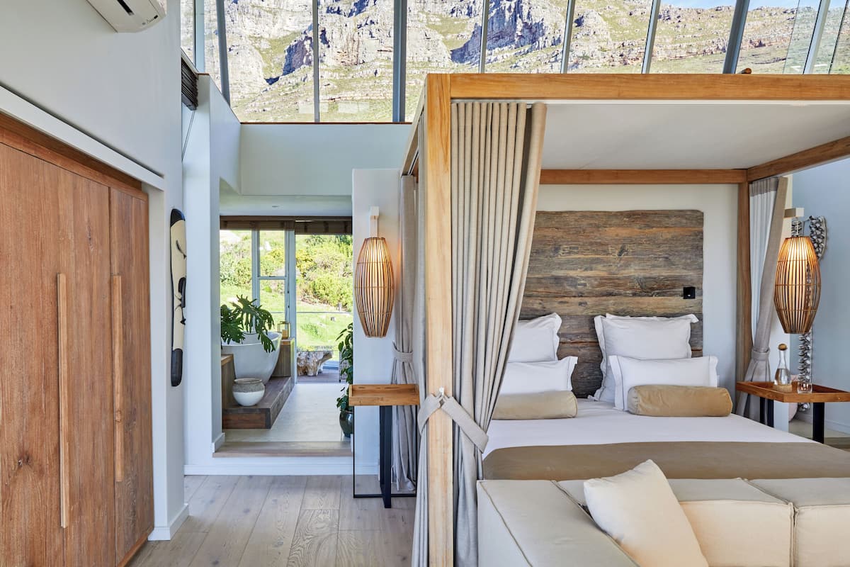 Ein modernes Schlafzimmer mit einem Holzkopfende, einem großen Bett und Blick ins Freie durch große Fenster.