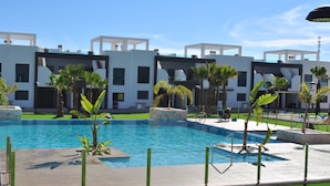 A modern hotel with a swimming pool, palm trees, and a clear blue sky. - Groundfloor Oasis Beach II La Zenia (Orihuela Costa)