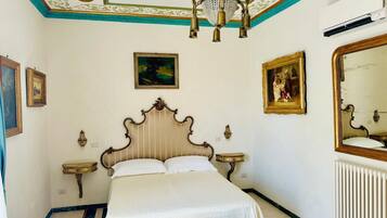 A bedroom with a large bed, ornate ceiling, and artwork on the walls.