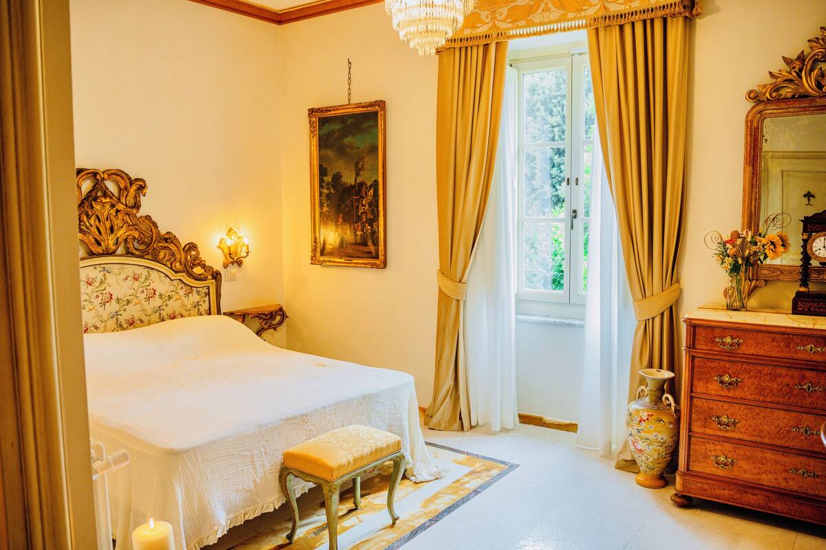 Une chambre à coucher avec un lit, une table de chevet, une commode, un vase et un tableau accroché au mur.