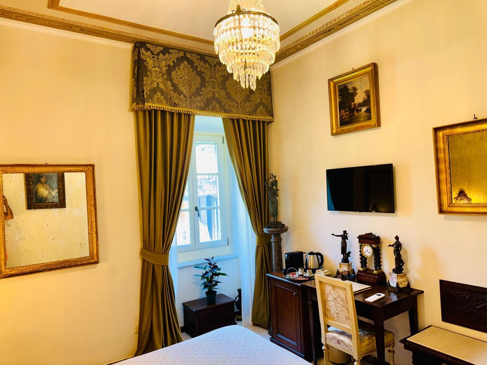 A hotel room with a bed, a desk, a chair, a television, and a chandelier.