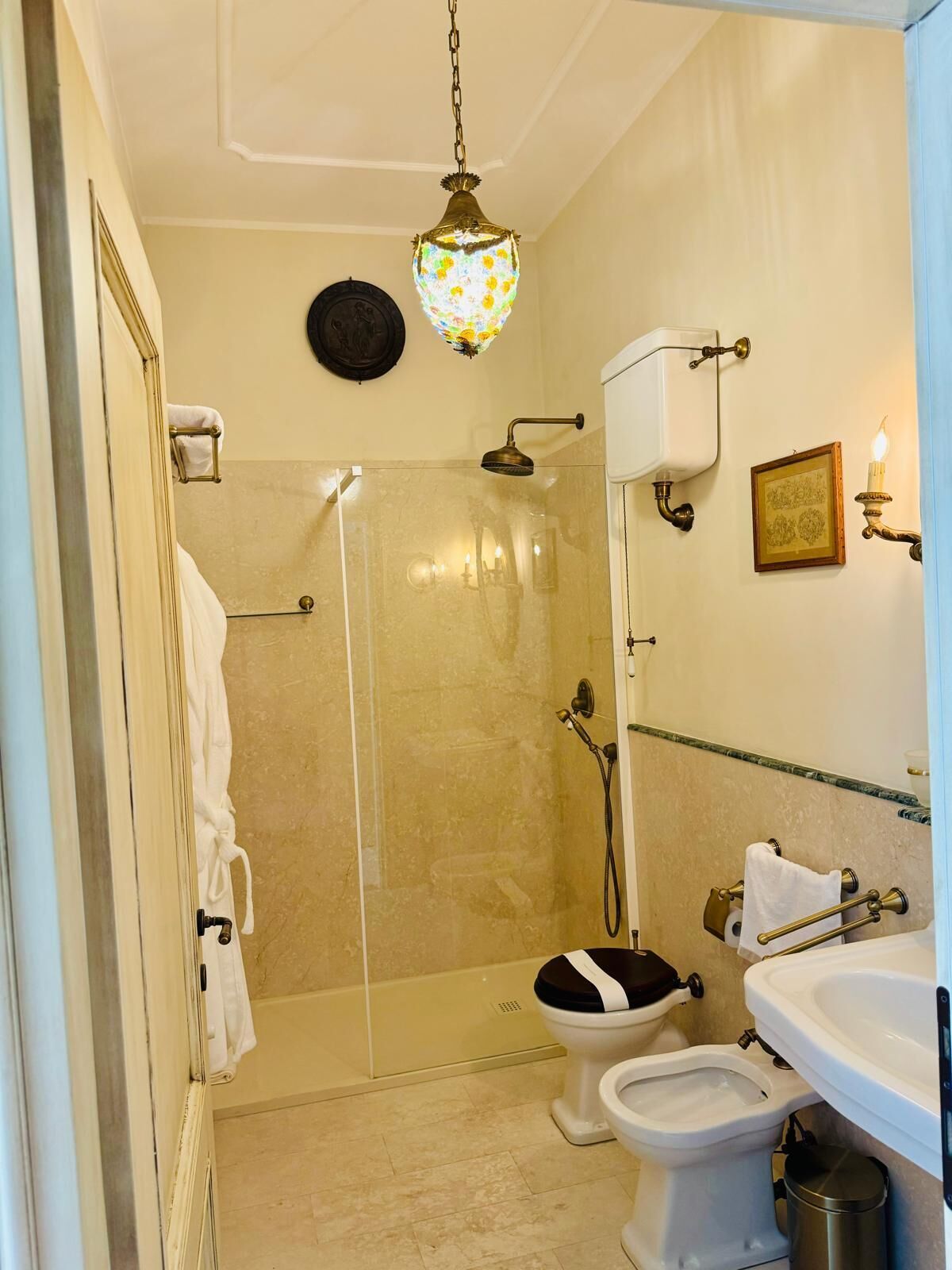 A bathroom with a glass-enclosed shower, a toilet, a sink, and a wall-mounted light fixture.