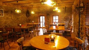 A rustic restaurant interior with stone walls, wooden tables, and hanging light fixtures.