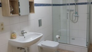 A bathroom with a glass shower enclosure, a sink, a toilet, and a wooden medicine cabinet.
