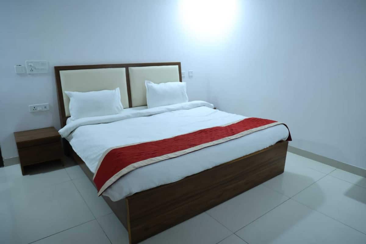 A neatly made bed with a wooden headboard, white bedding, and a red accent.