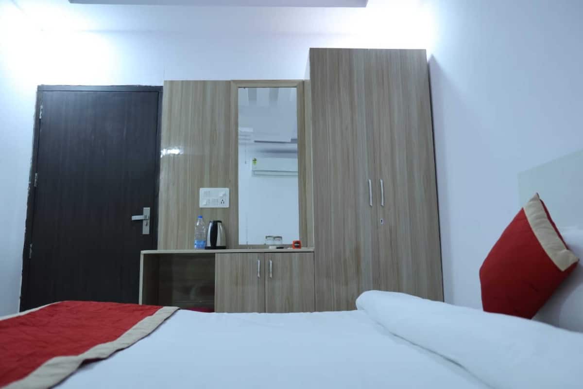 A hotel room with a bed, a wardrobe, a mirror, and a small table with a kettle and a bottle.