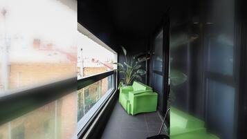 A narrow balcony with a green planter and a window overlooking a cityscape.