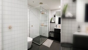 A modern bathroom with white tiled walls, a glass shower enclosure, a toilet, a sink, and a mirror.