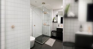 Ein modernes Badezimmer mit weißen Fliesen, einer Glasdusche, einer Toilette, einem Waschbecken und einem Spiegel.