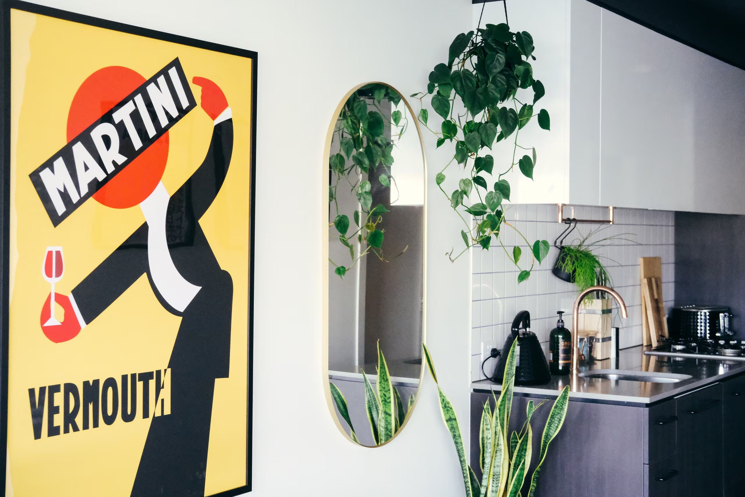 A kitchen with a large framed poster, a mirror, and potted plants.
