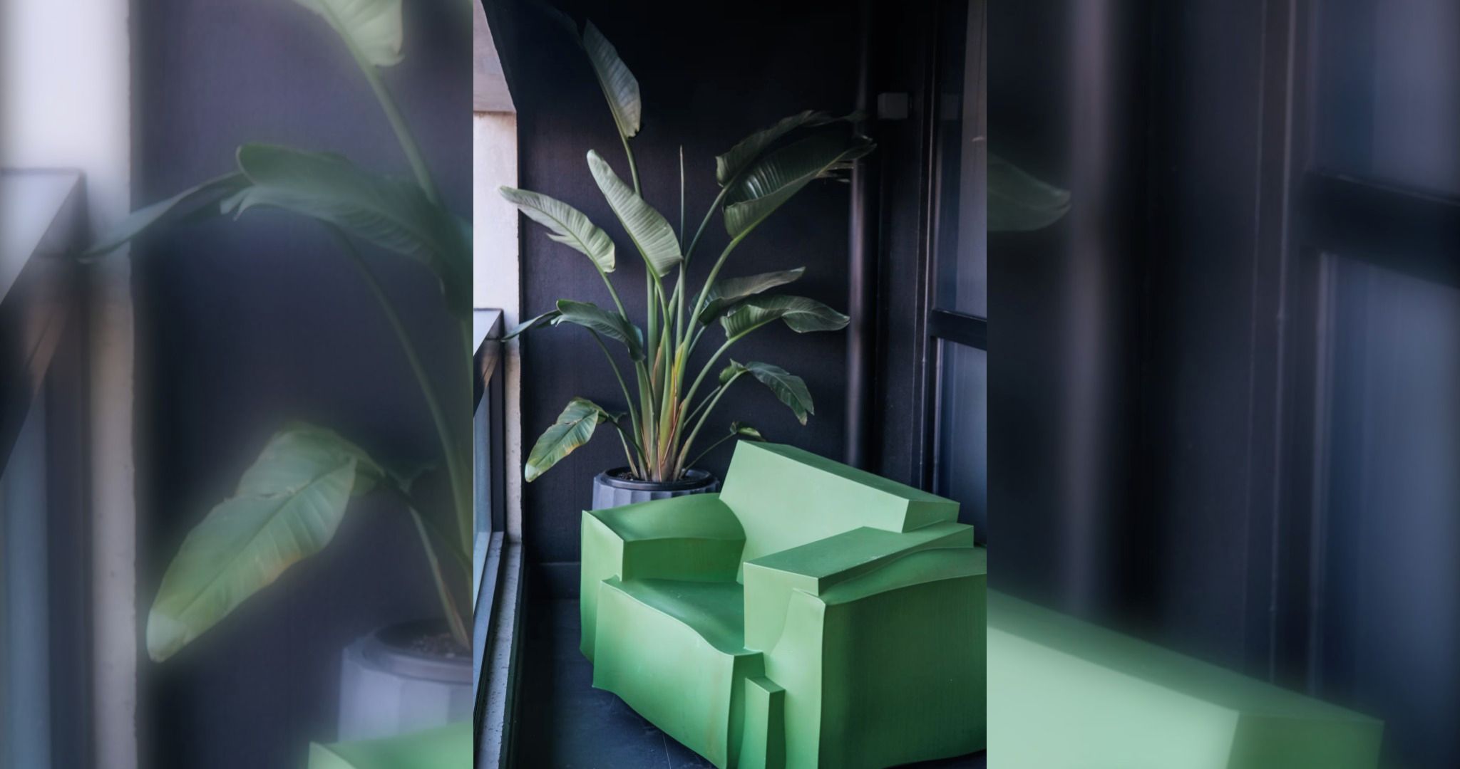 A modern interior with a potted plant and geometric green furniture against a dark wall.