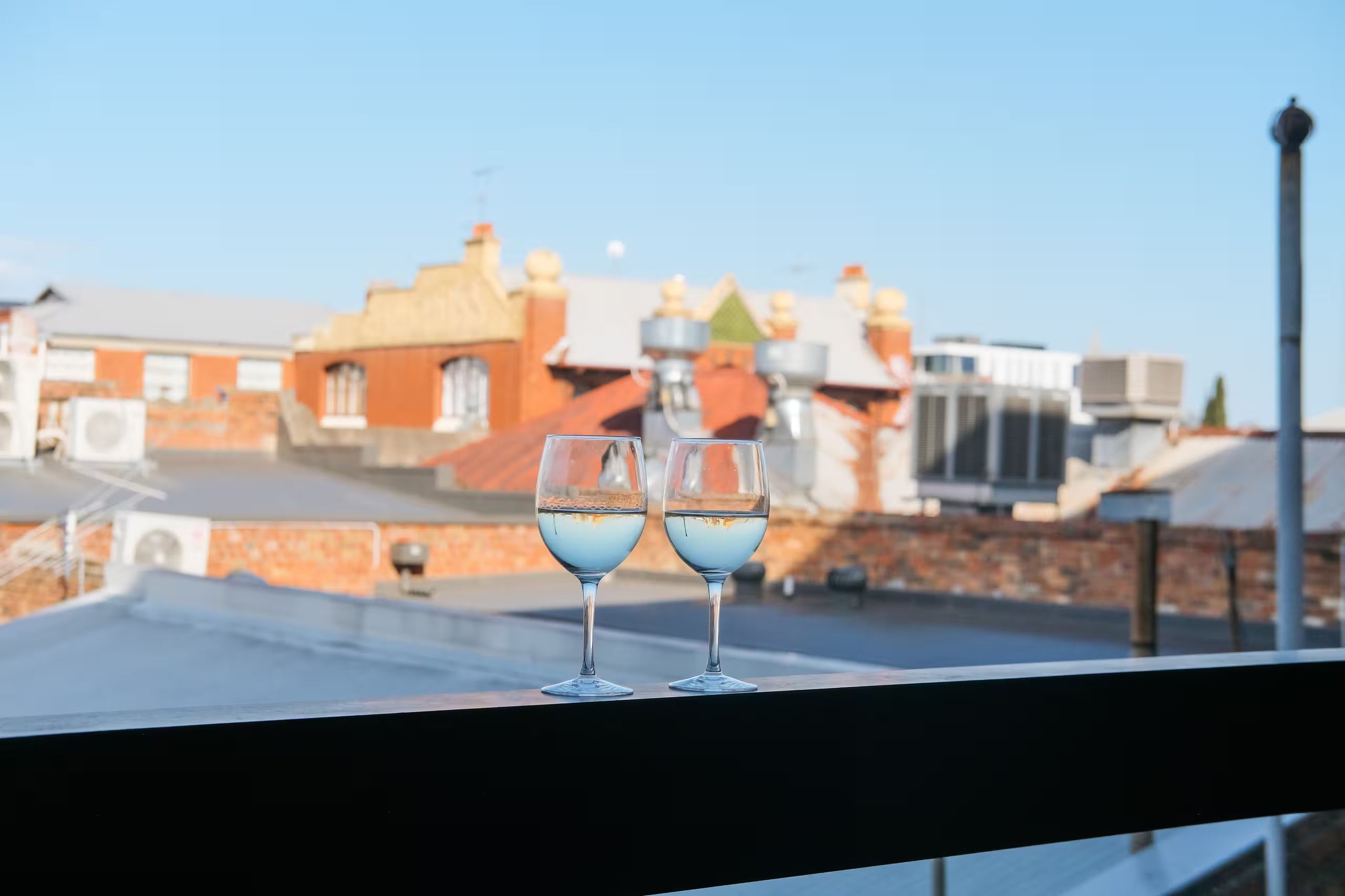 To glas hvidvin på en balkon med udsigt til bygninger.